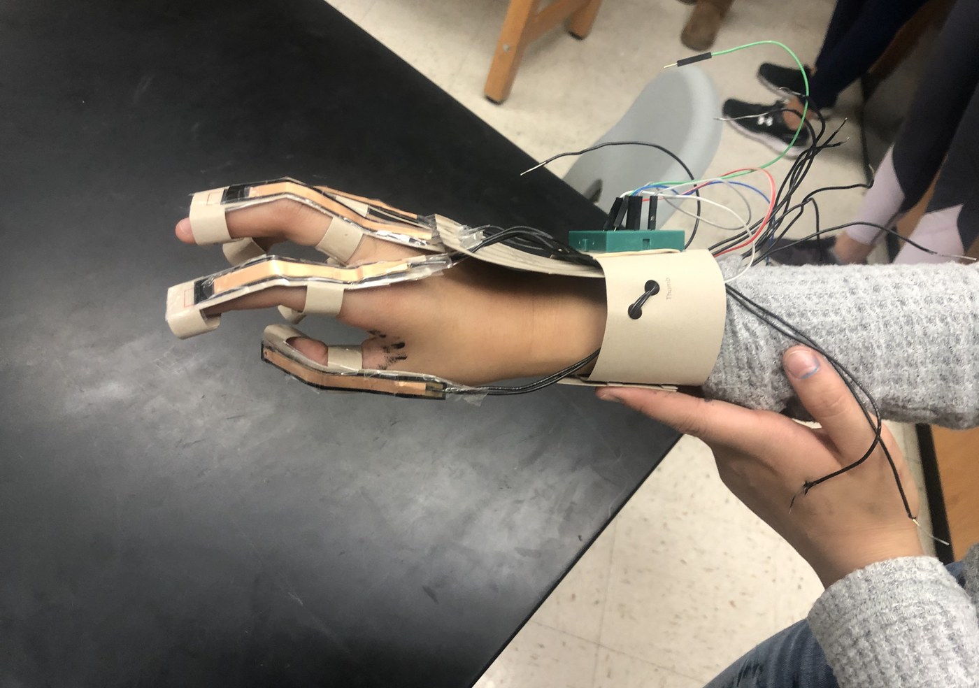 A student-built assistive hand device wired to a sensor board, held up in the lab