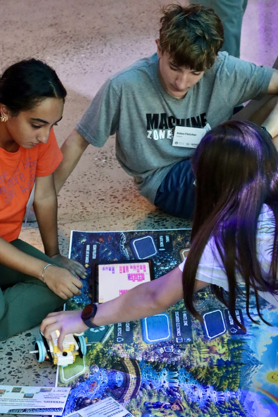Three students programming a robot together on a sustainable-city floor map