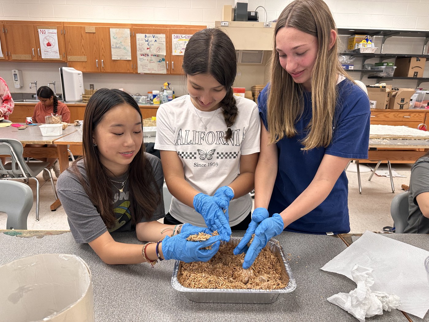 Three Orblynx students packing mycelium substrate into a tray during a biomaterials session